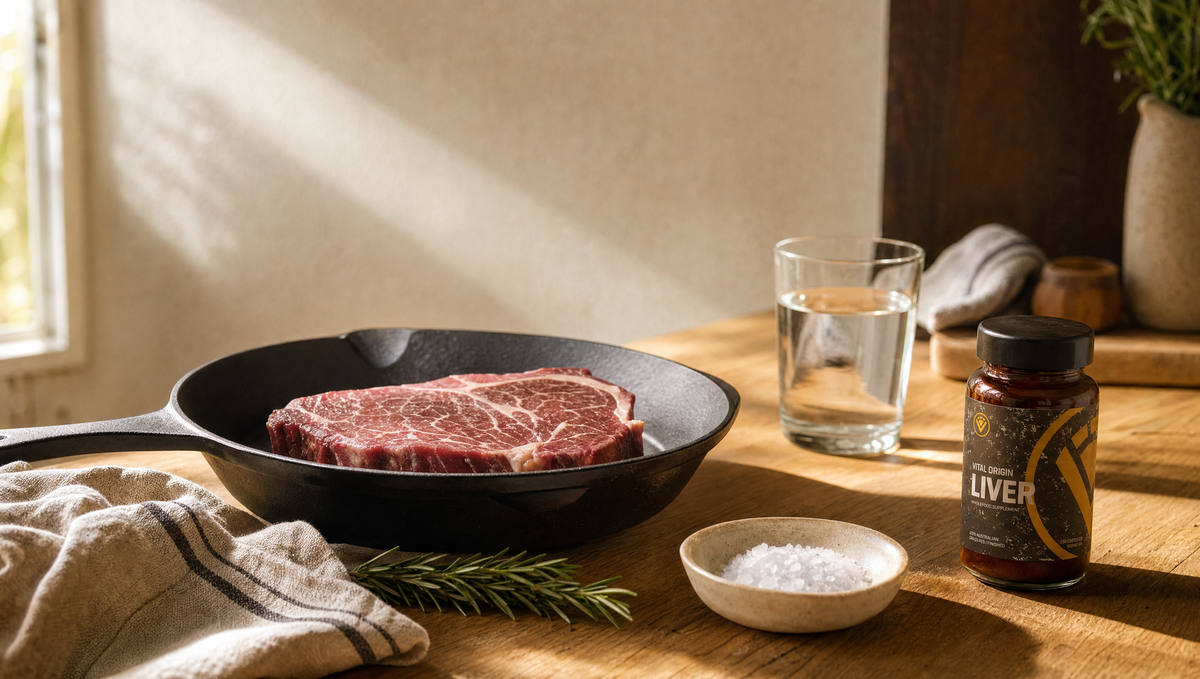 Steak resting in a cast-iron pan with coarse sea salt, a glass of water and Vital Origin Beef Liver Capsules on an Australian kitchen benchtop in warm morning light