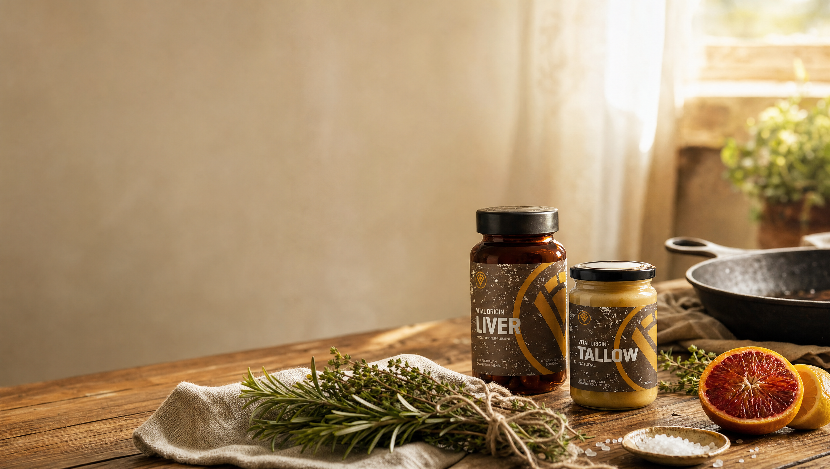 Beef liver capsules and grass-fed beef tallow resting together on a timber farmhouse table with fresh herbs and citrus in morning light, representing a staged nose-to-tail nutrition routine